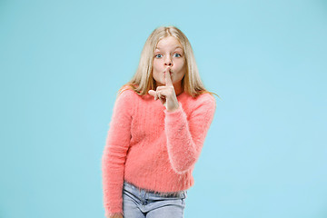 Image showing The young teen girl whispering a secret behind her hand over blue background