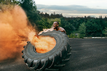 Image showing Handsome muscular man flipping big tire outdoor.