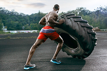 Image showing Handsome muscular man flipping big tire outdoor.