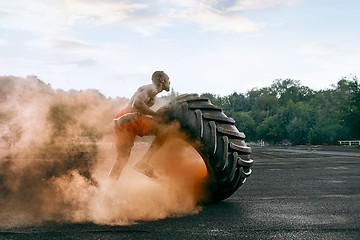 Image showing Handsome muscular man flipping big tire outdoor.