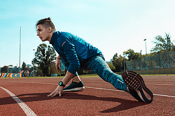 Image showing Man runner stretching legs preparing for run training on stadium tracks doing warm-up