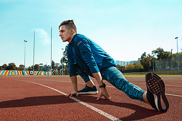 Image showing Man runner stretching legs preparing for run training on stadium tracks doing warm-up