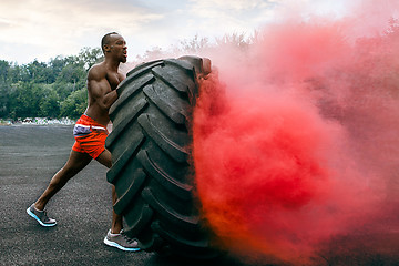 Image showing Handsome muscular man flipping big tire outdoor.