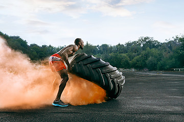 Image showing Handsome muscular man flipping big tire outdoor.