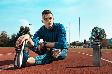 Image showing Man runner stretching legs preparing for run training on stadium tracks doing warm-up