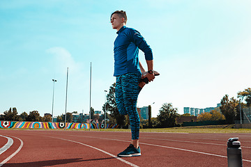 Image showing Man runner stretching legs preparing for run training on stadium tracks doing warm-up