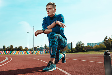 Image showing Man runner stretching legs preparing for run training on stadium tracks doing warm-up