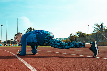 Image showing Man runner stretching legs preparing for run training on stadium tracks doing warm-up