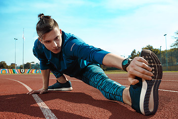 Image showing Man runner stretching legs preparing for run training on stadium tracks doing warm-up