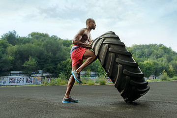 Image showing Handsome muscular man flipping big tire outdoor.