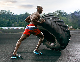 Image showing Handsome muscular man flipping big tire outdoor.