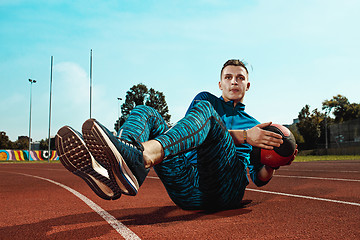 Image showing Man runner stretching legs preparing for run training on stadium tracks doing warm-up