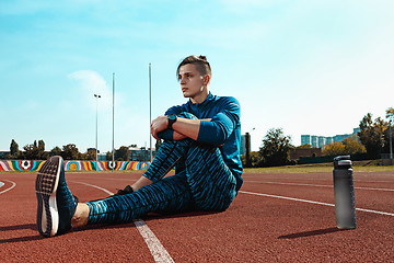 Image showing Man runner stretching legs preparing for run training on stadium tracks doing warm-up