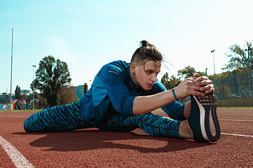 Image showing Man runner stretching legs preparing for run training on stadium tracks doing warm-up