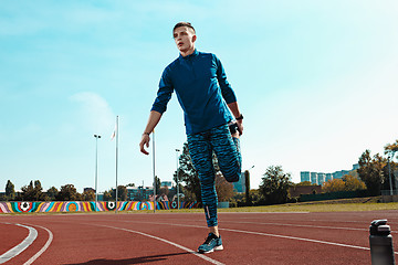 Image showing Man runner stretching legs preparing for run training on stadium tracks doing warm-up