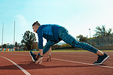 Image showing Man runner stretching legs preparing for run training on stadium tracks doing warm-up