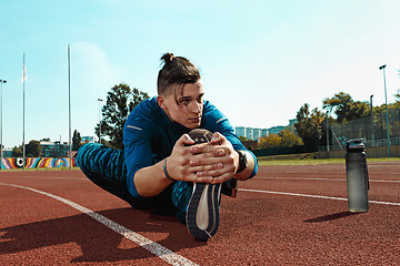 Image showing Man runner stretching legs preparing for run training on stadium tracks doing warm-up