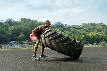 Image showing Handsome muscular man flipping big tire outdoor.