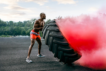 Image showing Handsome muscular man flipping big tire outdoor.