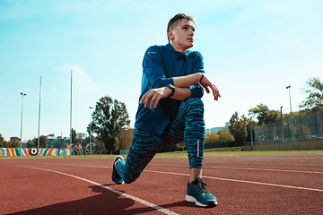 Image showing Man runner stretching legs preparing for run training on stadium tracks doing warm-up