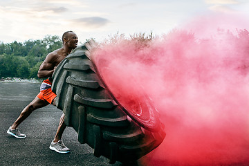 Image showing Handsome muscular man flipping big tire outdoor.