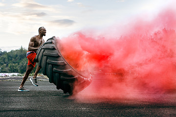 Image showing Handsome muscular man flipping big tire outdoor.