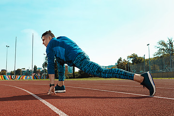 Image showing Man runner stretching legs preparing for run training on stadium tracks doing warm-up