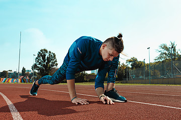 Image showing Man runner stretching legs preparing for run training on stadium tracks doing warm-up