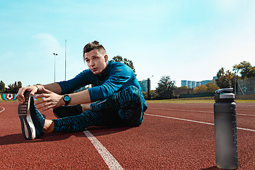 Image showing Man runner stretching legs preparing for run training on stadium tracks doing warm-up