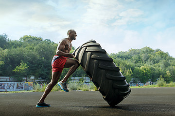 Image showing Handsome muscular man flipping big tire outdoor.