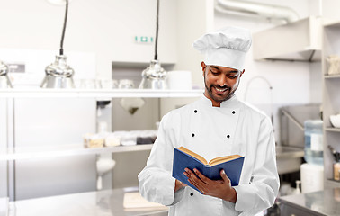 Image showing happy indian chef reading cookbook at kitchen