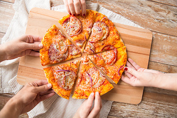 Image showing close up of hands sharing pizza on wooden table