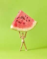 Image showing Fresh ripe peace of watermelon in the hands of wooden mannequin model.