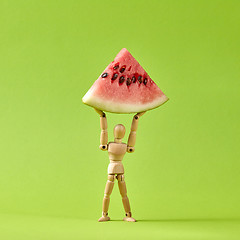 Image showing Energy wooden mannequin model holds slice of ripe water melon.