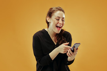 Image showing Young beautiful woman using mobile phone studio on gold color background