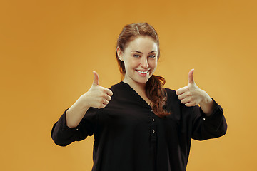 Image showing The happy business woman standing and smiling against gold background.