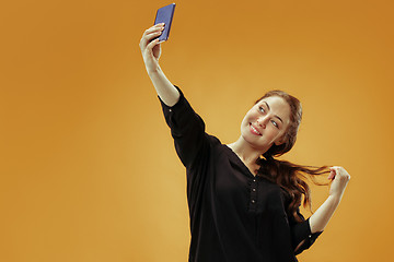 Image showing Portrait of a happy smiling casual girl showing blank screen mobile phone isolated over gold background