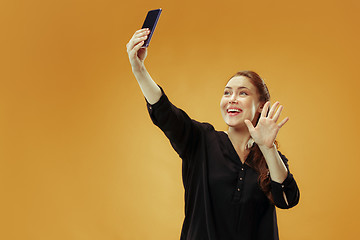 Image showing Portrait of a happy smiling casual girl showing blank screen mobile phone isolated over gold background