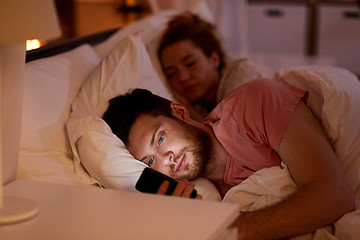 Image showing man using smartphone while girlfriend is sleeping