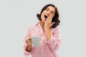 Image showing happy yawning young woman in pajama with coffee