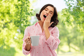 Image showing happy yawning young woman in pajama with coffee