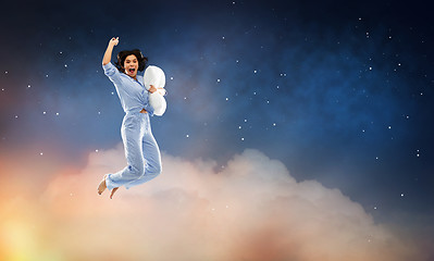 Image showing happy woman in blue pajama jumping with pillow