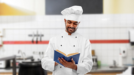 Image showing happy indian chef reading cookbook at kitchen