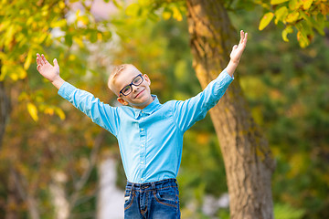 Image showing Hilarious seven-year-old boy gleefully raised his hands up in autumn city park