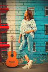 Image showing Beautiful brunette woman in blue jeans with a guitar