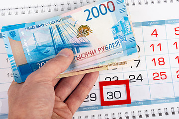 Image showing Hand holds wad of money over calendar number 30