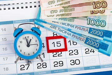 Image showing The calendar marks the fifteenth, with banknotes and watches lying next to