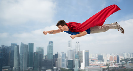 Image showing man in red superhero cape flying in air over city