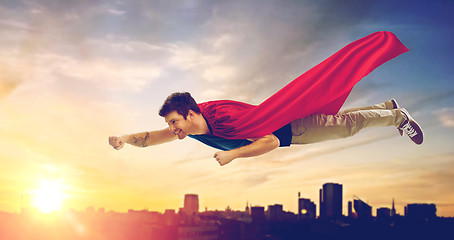 Image showing man in superhero cape flying over sunset in city