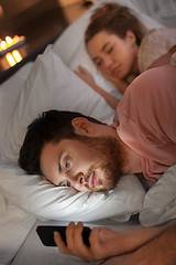 Image showing man using smartphone while girlfriend is sleeping